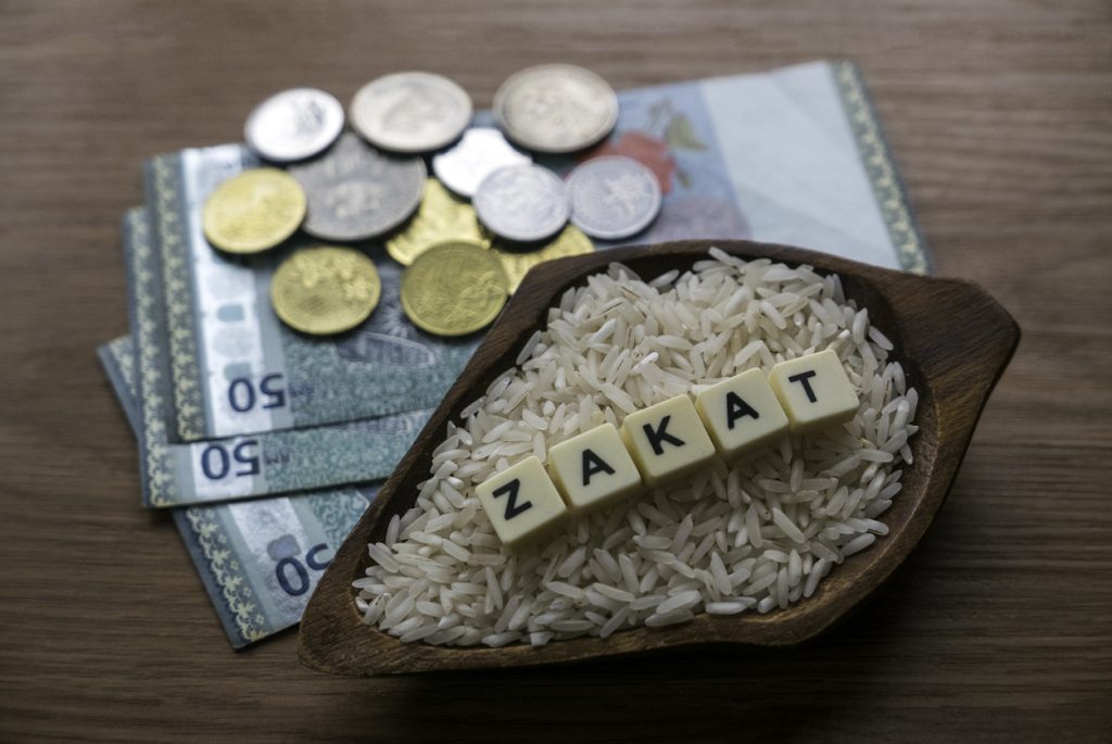Concept of zakat in Islam religion. Selective focus of money and rice with alphabet of zakat on wooden background.
