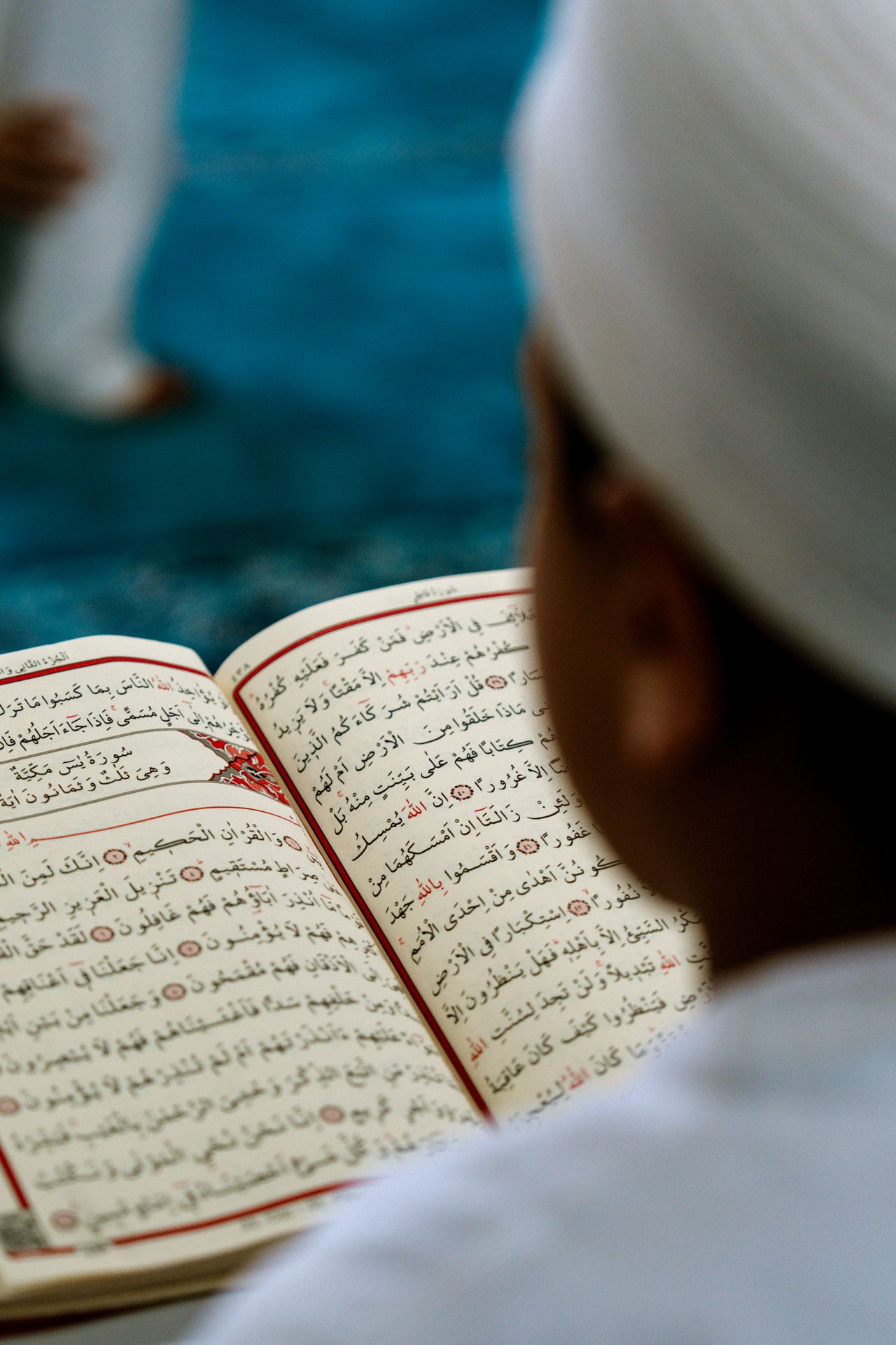 A young student reading closely from the Qur’an during an evening recitation lesson