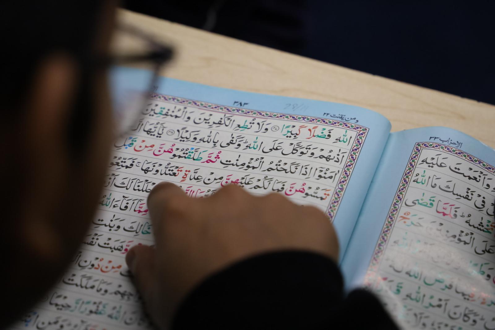 A child reading the Qur’an over the shoulder of a guiding teacher